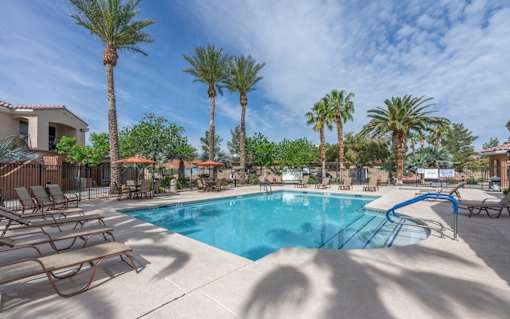 A pool surrounded by palm trees and lounge chairs.
