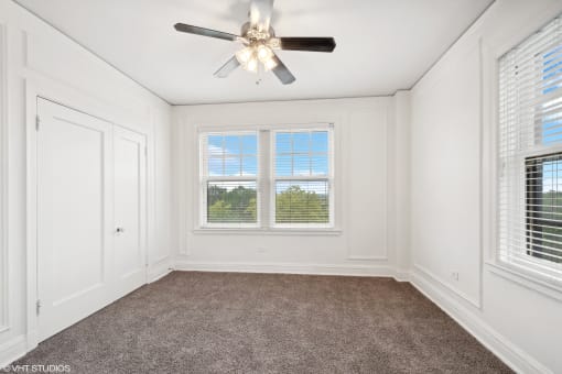 an empty bedroom with a ceiling fan and two windows  at The Embassy in St. Louis, 63108