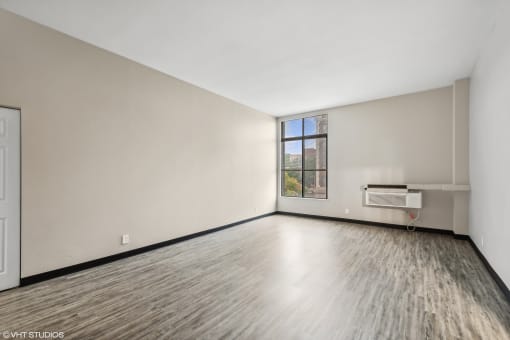 an empty living room with white walls and wood floors and a window at Delmar Loop Apartments, St. Louis, MO, 63112