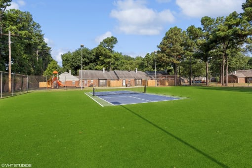 a tennis court with a blue court in the middle of a grass field at The Birches Apartment Homes, Memphis, Tennessee