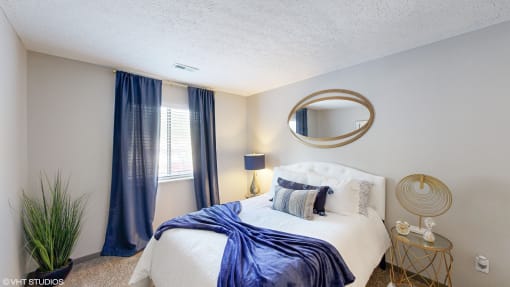 a bedroom with a white bed and blue curtains at Silvertree at Little Turtle Apartments, Westerville, OH