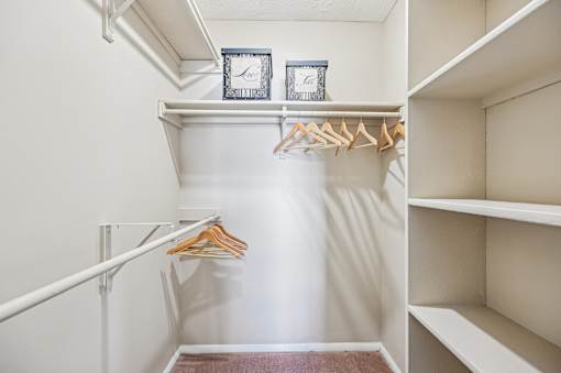 A white closet with a hanger and two clocks on the shelf.