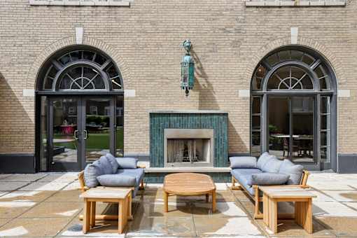 A fireplace with a wooden mantle and two couches in front of a building with arched windows.