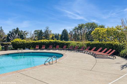 A pool surrounded by red lounge chairs and green trees at Island Club Apartments, Ohio