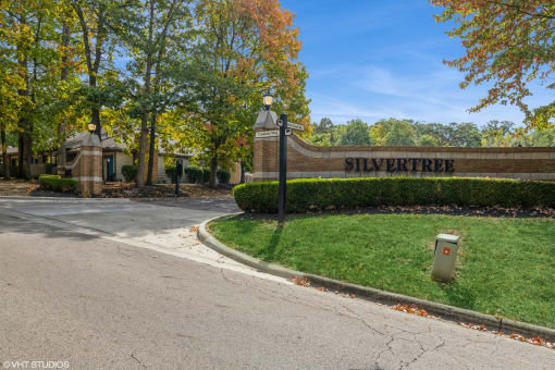 a brick building with a street sign in front of a green lawn and trees at Silvertree at Little Turtle Apartments, Westerville