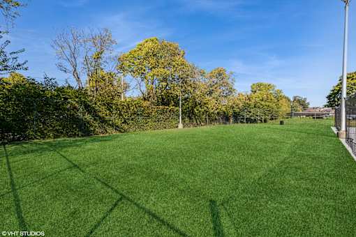 A grassy field with trees in the background and a fence on the right side at Island Club Apartments, Ohio