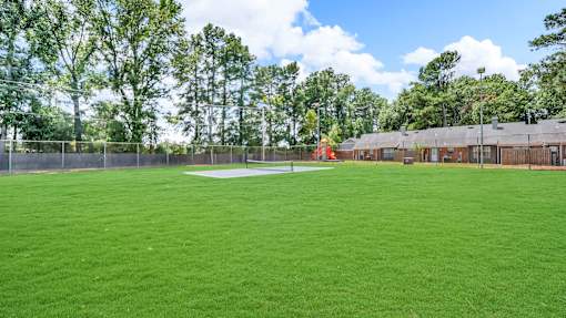 A large grassy field with trees in the background and a building to the right.