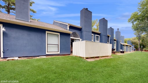 a row of blue houses with a yard and green grass at The Vale Apartments and Townhomes, Cordova, TN
