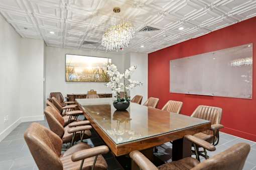 A long wooden table is surrounded by chairs in a room with a chandelier hanging from the ceiling.
