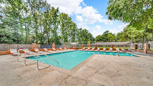 A large outdoor swimming pool surrounded by trees and lounge chairs.