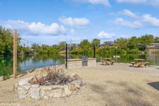 a fire pit next to a lake with picnic tables at Runaway Bay Apartments, Ohio