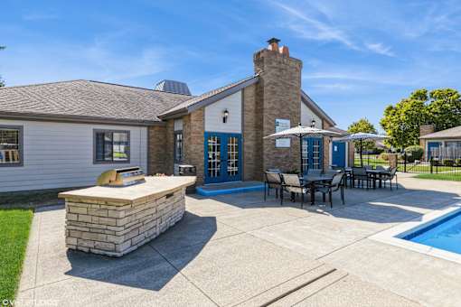 A house with a stone fireplace and a pool in the backyard at Karric Place of Dublin Apartments, Dublin, Ohio
