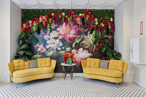 Two yellow couches in front of a floral mural.