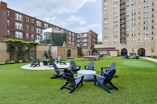 A lawn with chairs and tables is surrounded by buildings.