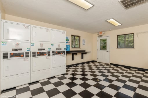 the laundry room has a checkered floor and white washers and dryers at Silvertree at Little Turtle Apartments, Westerville