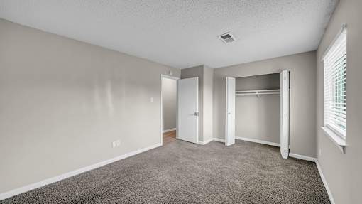 A room with a carpeted floor and a window with blinds. at The Stella Apartments, Memphis, Tennessee