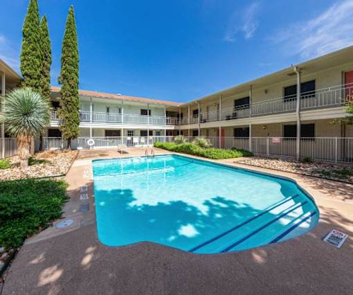 A swimming pool in front of a building with trees and bushes around it.