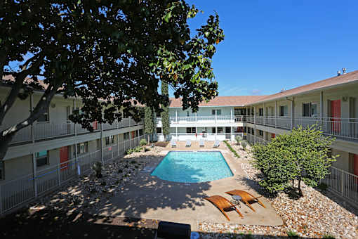 A pool surrounded by trees and chairs in a courtyard.