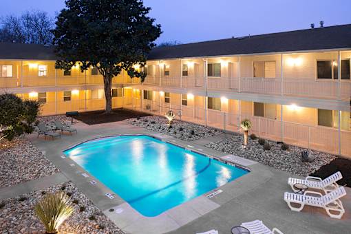 A swimming pool surrounded by white lounge chairs and a tree.