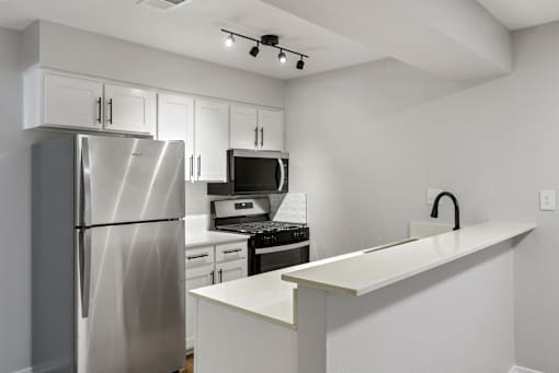 A kitchen with a refrigerator, microwave, oven, and a counter.