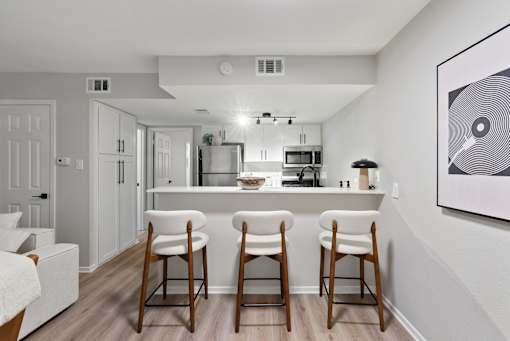A kitchen with white cabinets and a white fridge with a bar area in front.