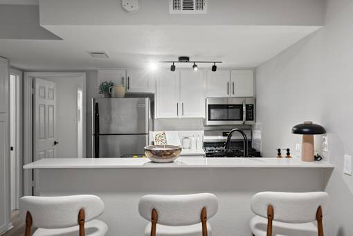 A modern kitchen with white chairs and appliances.