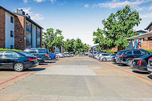 A parking lot with cars parked in rows and apartment buildings in the background at Water Ridge Apartments , Irving, Texas