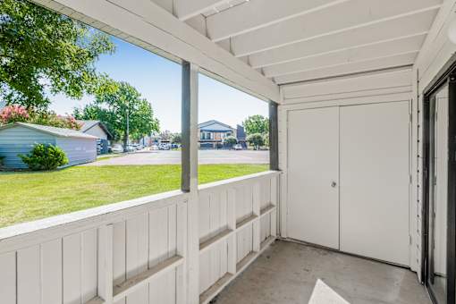A white wooden balcony with a white door and a window overlooking a green lawn and a blue house at Water Ridge Apartments , Texas, 75061