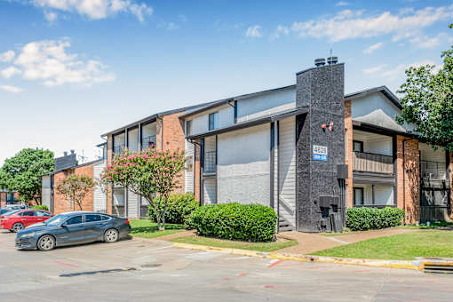 A grey car is parked in front of a building with a blue sign on it at Water Ridge Apartments , Irving
