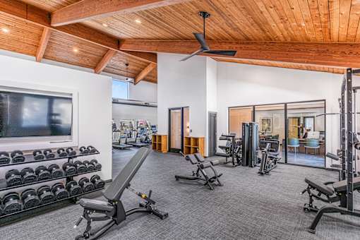 A spacious home gym with a variety of equipment including dumbbells, weight machines, and a bench press at Water Ridge Apartments , Irving, TX
