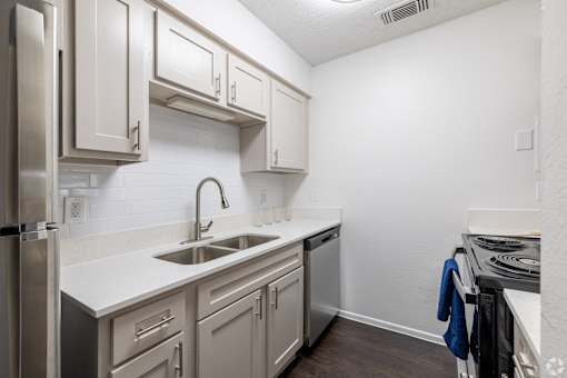 A kitchen with a stainless steel refrigerator, a white sink, and a white countertop.