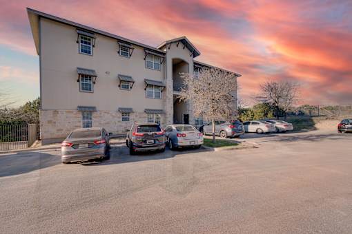 A parking lot with cars and a building in the background at Logan Ridge Apartments, San Marcos, 78666