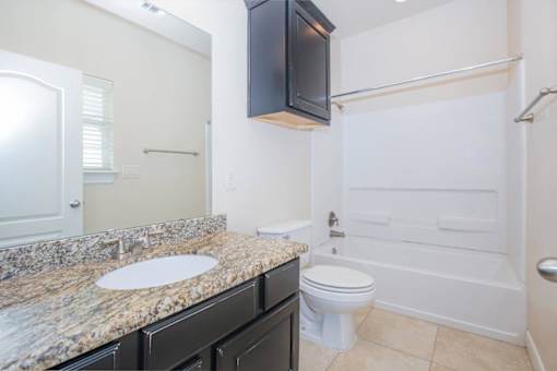 A bathroom with a granite countertop and white fixtures at Logan Ridge Apartments, San Marcos