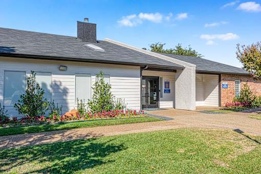 A small building with a grey roof and a white wall with a blue sign on it at Water Ridge Apartments , Texas