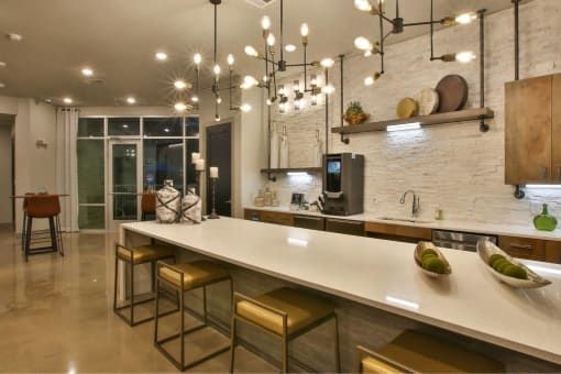 a kitchen with a long counter and chairs at The Grand at Stonecreek, San Marcos, TX
