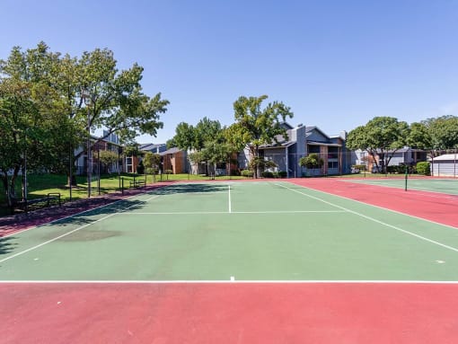 a tennis court with trees and apartments in the background at Water Ridge Apartments, Irving, 75061