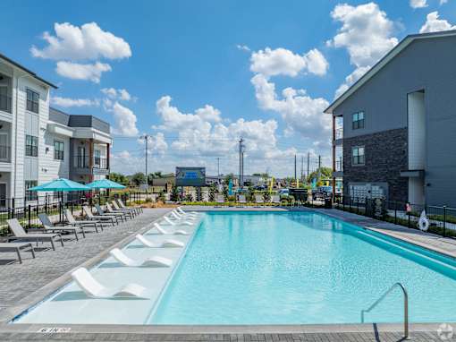 A large swimming pool with lounge chairs and umbrellas in front of a building at The Virginia Apartments , Seguin, TX, 78155