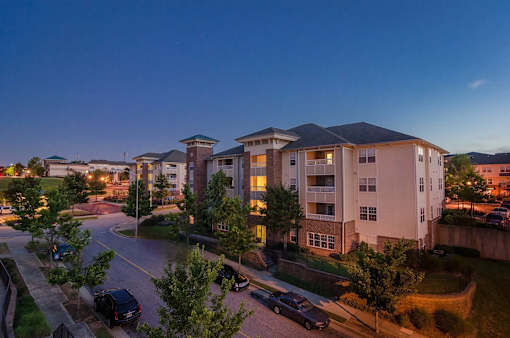 Apartment complex with cars parked in front and trees in the foreground.