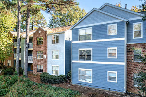 A blue building with white windows is situated next to a green building with red brick.