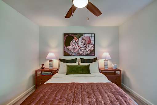 A bedroom with a bed, two lamps, and a painting on the wall.