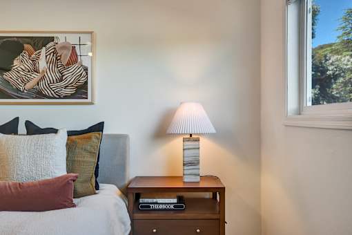 A bedroom with a bed, a nightstand with a lamp and a painting on the wall.