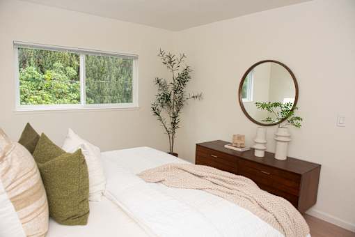 A bedroom with a bed, pillows, a mirror, and a plant.
