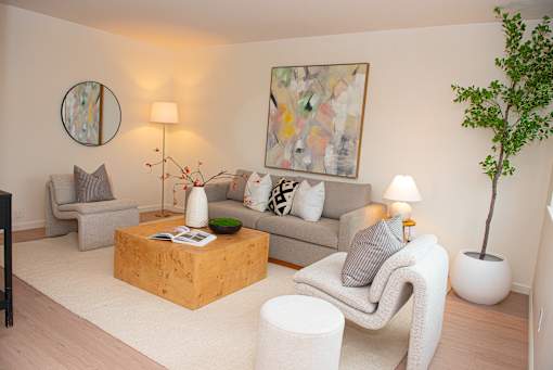 A living room with a grey couch, a white chair, a wooden coffee table, and a painting on the wall.
