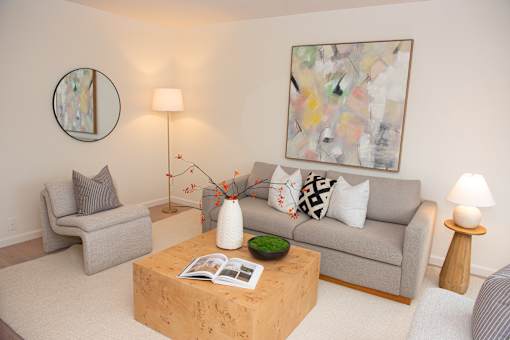 A living room with a grey couch, a wooden coffee table, and a painting on the wall.