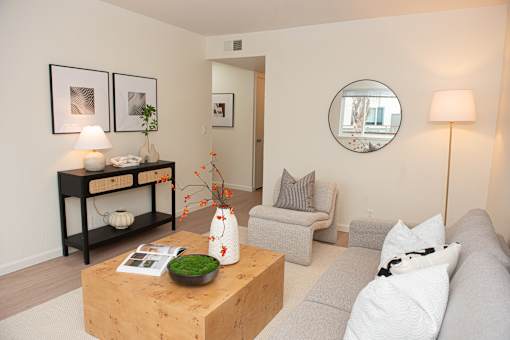 A living room with a grey couch, a wooden coffee table, and a round mirror on the wall.