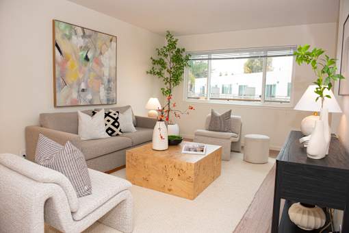 A living room with a grey couch, a white chair, a wooden coffee table, and a painting on the wall.