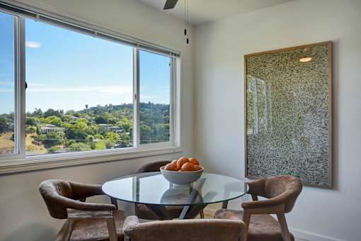 A dining room with a glass table and chairs and a view of the outdoors through the window.