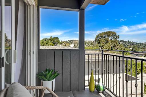 A balcony with a chair, a table, and a potted plant overlooks a residential area.
