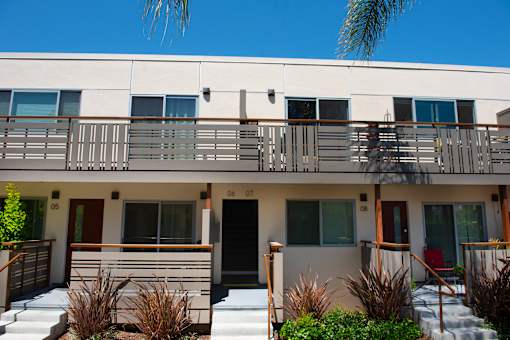 A white building with a balcony and a red door.