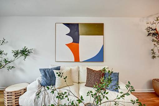 A living room with a white couch and a colorful abstract painting above it.